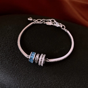 Macro shot of silver bracelet with three zircon rings on dark textured fabric