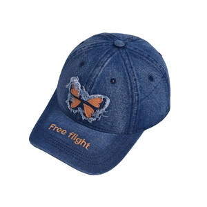 Detail of blue denim baseball cap featuring butterfly patch and Free Flight embroidery