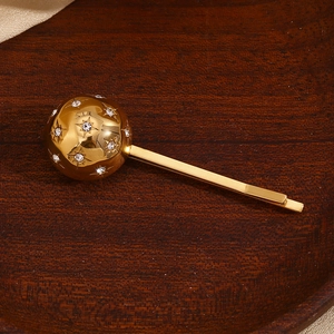 Detail einer 18K vergoldeten Haarspange mit einer Sternenkugel aus Strass auf Holz