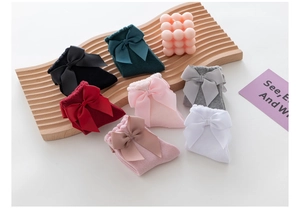 Macro detail of seven colorful girls' cotton socks with large ribbon bows in various shades