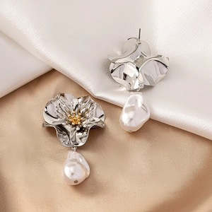 Close-up of floral metal earrings with golden stamens and baroque pearl drops