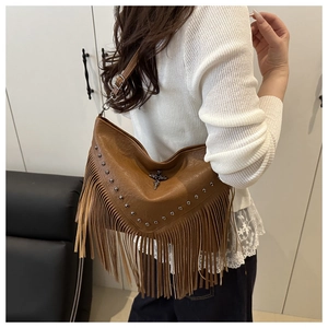 Detail of brown vintage shoulder bag featuring rivets, fringes and a metal cross ornament