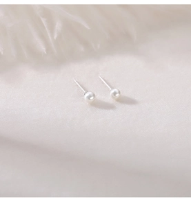 Detailed macro view of S999 sterling silver pearl stud earrings on soft white fabric
