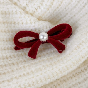 Close-up of a deep red velvet bow hair clip with a center pearl on white knit fabric