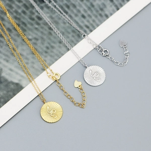 Detailed view of round serpent pendant necklaces in gold and silver finish with sunburst texture