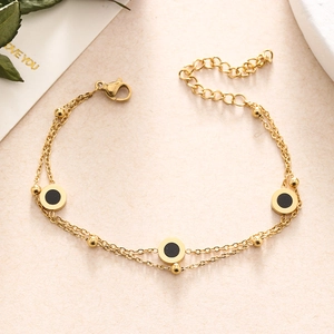 Detail view of a double-layer gold chain bracelet with black circular resin charms and beads