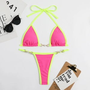 Bikini rose et vert avec anneaux dorés et perles posé à plat sur une surface blanche