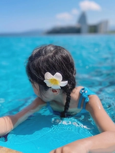 Close-up of a realistic white plumeria flower hair clip with a blue swimsuit background
