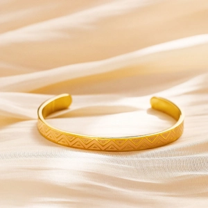 Detailed close-up of gold-plated open bangle with geometric triangle patterns on silk