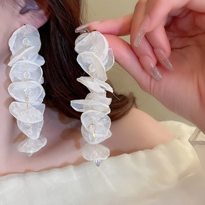 Detailed view of long tassel earrings with white organza petals and gold accents on model