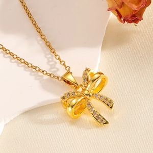 Close-up of a gold bow pendant necklace with sparkling zircons on white silk and dried flowers