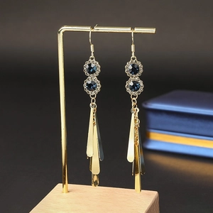 Detailed view of long gold tassel earrings with dark blue rhinestones on a display stand
