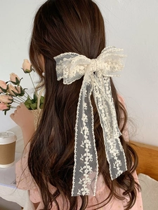 Detailed view of beige lace bow hair clip with floral embroidery on long streamers
