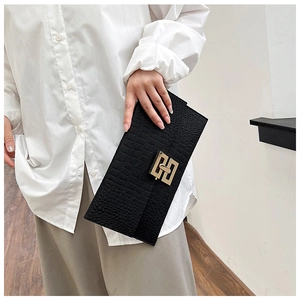 Detail of black crocodile pattern clutch bag with gold geometric metal hardware in hand