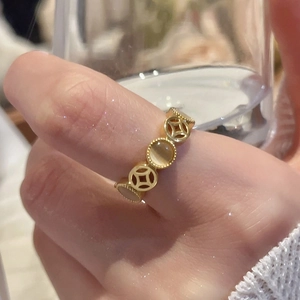 Close-up of golden geometric hollow coin ring with opal stone worn on finger