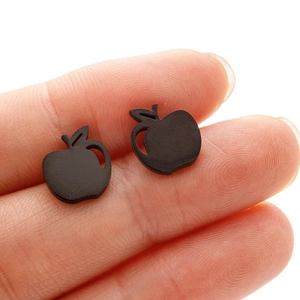 Macro view of matte black apple-shaped stainless steel stud earrings held by hand