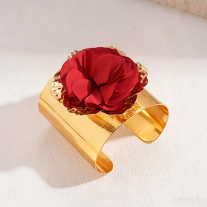 Detail of a wide gold cuff bracelet featuring a large 3D red fabric flower decoration