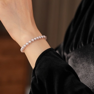 Detailed view of high-luster lavender pearl beaded bracelet worn on a velvet sleeve