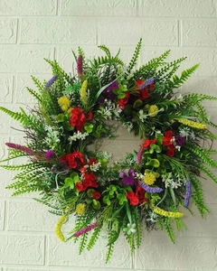 Detail of colorful artificial wildflower wreath with red and yellow ranunculus on white wall