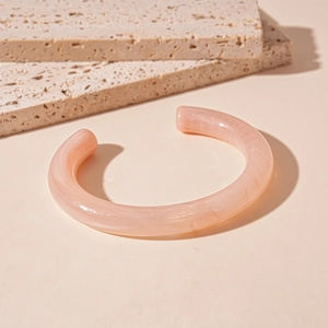 Detail view of pink marble pattern acrylic open cuff bracelet on beige stone background