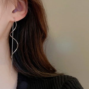 Close-up of silver wavy tassel threader earrings worn by a model in soft lighting