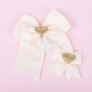 Detail of beige grosgrain bow hair clips with gold glitter heart centers on pink backdrop