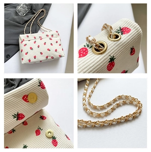 Detail view of cream corduroy crossbody bag with strawberry print and gold chain strap