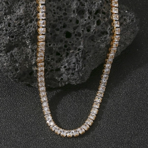 Macro shot of gold tennis necklace with square zircons on black volcanic rock base