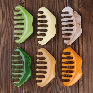 Detailed collection of colorful wide-tooth scalp massage combs and gua sha tools on wood