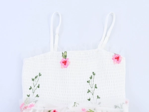 Détail du haut blanc smocké avec broderie florale délicate et fines bretelles