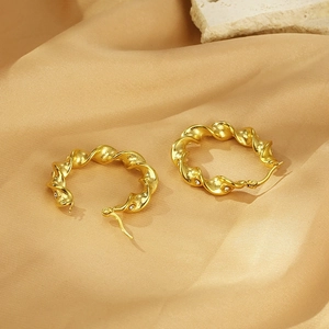 Detail of twisted gold hoop earrings with small white zircons on premium silk background