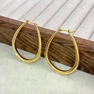Polished gold teardrop hoop earrings on a wooden jewelry display with a minimalist design