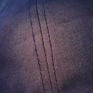 Macro detail showing high-quality triple-needle stitching on washed denim baseball cap fabric