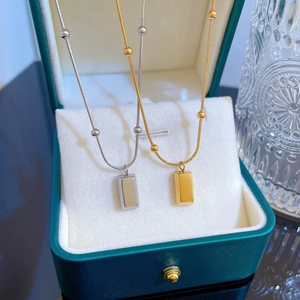 Gold and silver brick pendant necklaces with bead chain detail in a green jewelry box