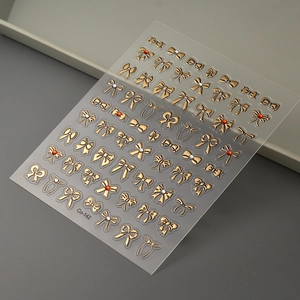 Detail of 3D metallic gold bow nail stickers with small red rhinestones and relief texture