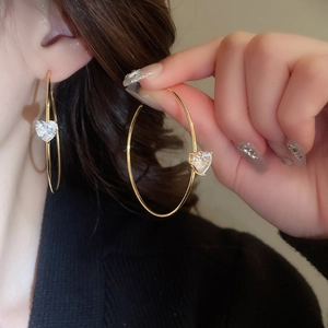 Gros plan d'une créole en C dorée avec pendentif coeur en zircon sur le mannequin