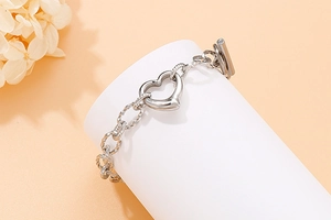 Detail of silver heart charm bracelet with OT buckle on a cylindrical prop and dry flowers