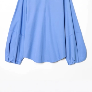 Chemisier en popeline bleu clair avec manches ballons et ourlet arrondi sur fond blanc