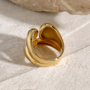 Macro shot of gold stainless steel organic curved ring on white natural stone