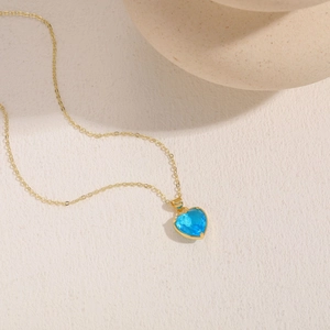 Artistic close-up of a gold chain necklace featuring a clear blue heart-shaped crystal
