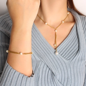 Detail of Y-shaped gold pearl necklace and bracelet set worn on a grey sweater