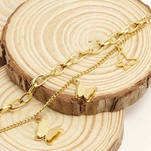Detail of gold double-layer chain bracelet with textured butterfly pendants on wood