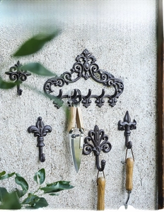 Detail of vintage cast iron fleur-de-lis wall hooks holding gardening tools on stone wall