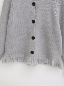 Detail of grey knitted cardigan showing black buttons, fringe hem, and soft woven texture