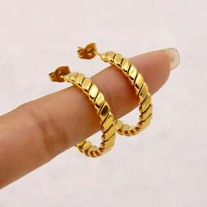 Polished gold twist hoop earrings shown on a hand to demonstrate size and style
