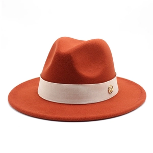 Macro view of burnt orange wool fedora hat with beige ribbon and gold logo metal buckle
