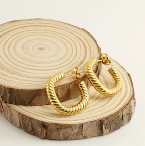 Macro view of 18K gold-plated twisted hoop earrings on natural wooden display stand