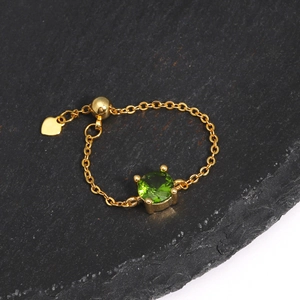 Detail of adjustable gold chain ring featuring green gemstone and heart pendant
