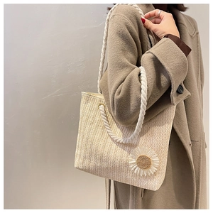 Detail of hand-woven straw tote with white cotton rope handles and a floral daisy accent