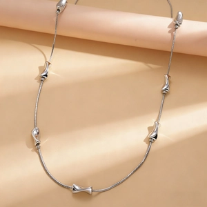 Detail of silver snake chain necklace with irregular liquid metal charms on beige props